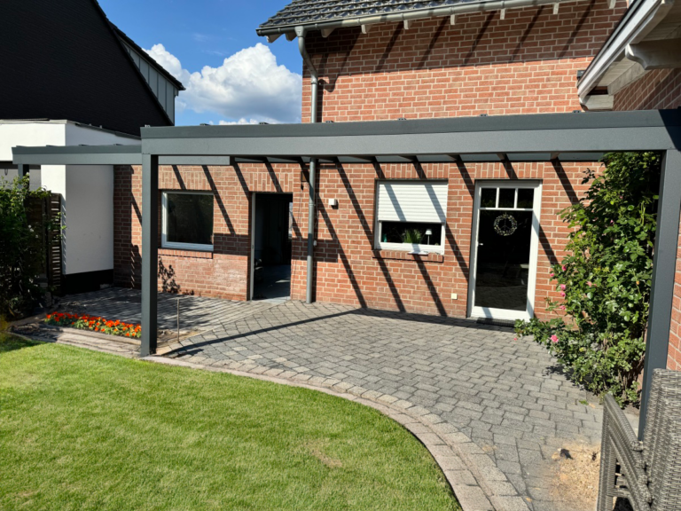 Ein Aluminium-Terrassendach an einem roten Backsteinhaus über einer gepflasterten Terrasse.